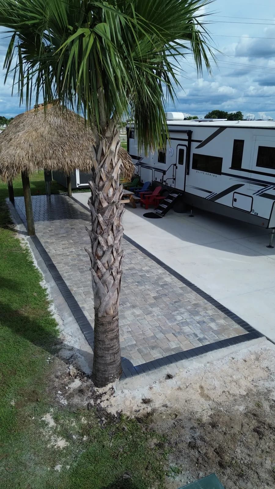 Paver pad with a dark border beside a sabal palm and a thatched tiki hut