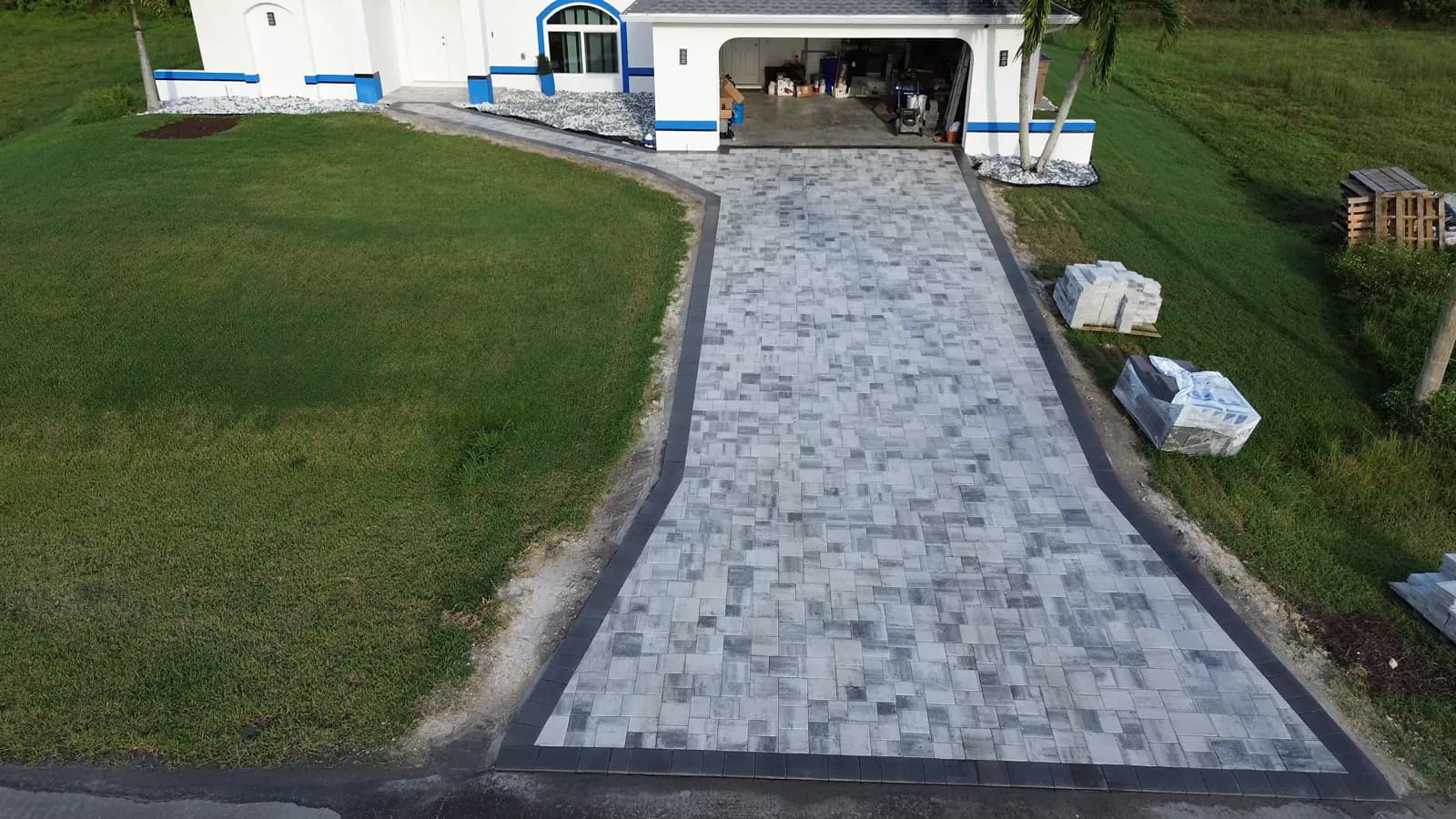 Aerial view of a new paver driveway with a dark soldier-course border leading to a garage